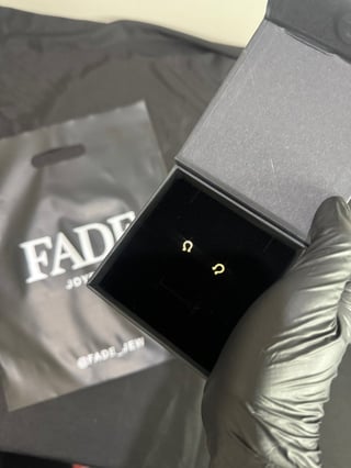 Open gray jewelry box with two small gold-toned earrings on black velvet