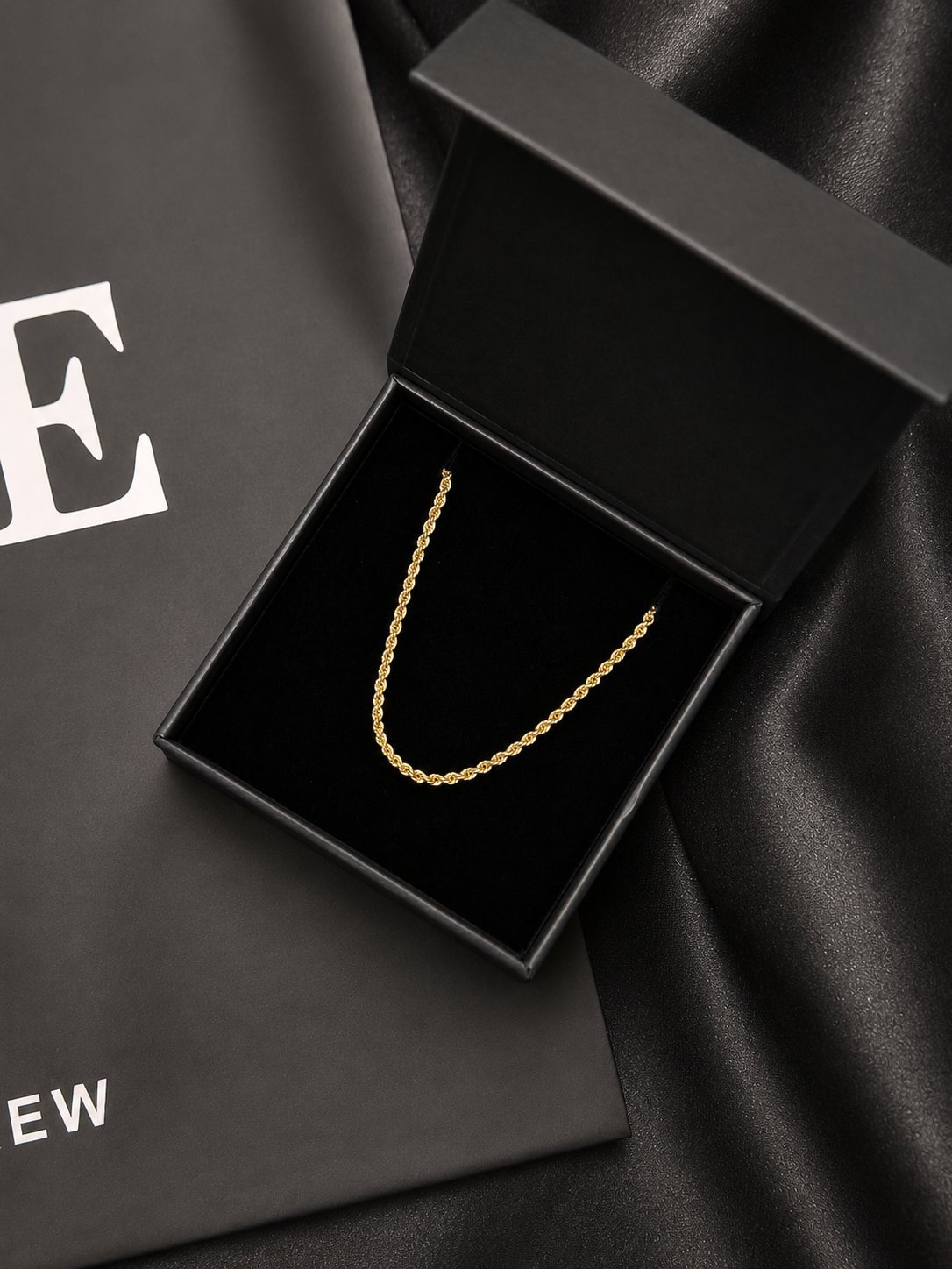 Gold rope chain necklace in open black gift box on dark silk fabric with branded packaging