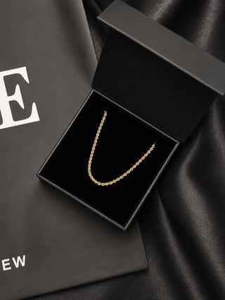 Gold rope chain necklace in open black gift box on dark silk fabric with branded packaging