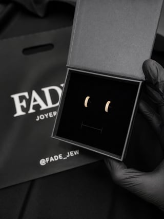 Pair of gold crescent moon stud earrings in an open jewelry box, held by a hand wearing black gloves