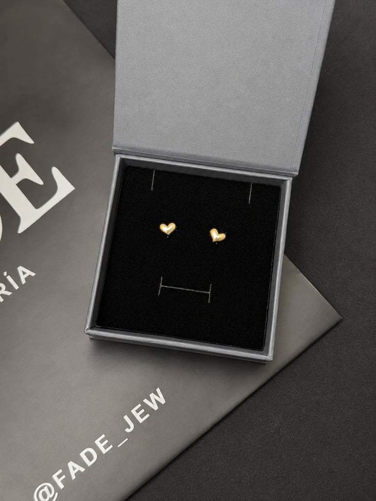 Pair of small gold heart-shaped stud earrings displayed on a black jewelry stand in an open gift box