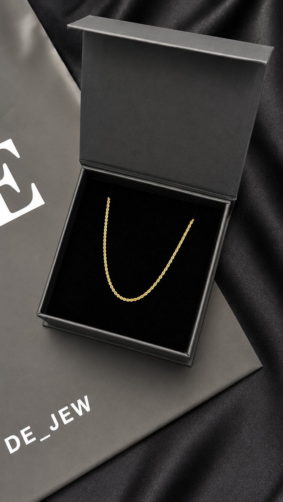 Gold chain necklace displayed in an open black luxury gift box on a dark fabric background