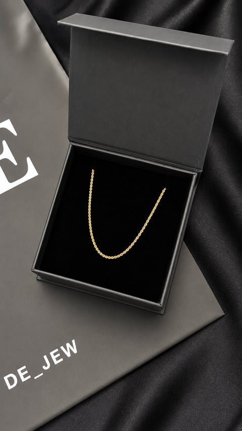 Gold chain necklace displayed in an open black luxury gift box on a dark fabric background