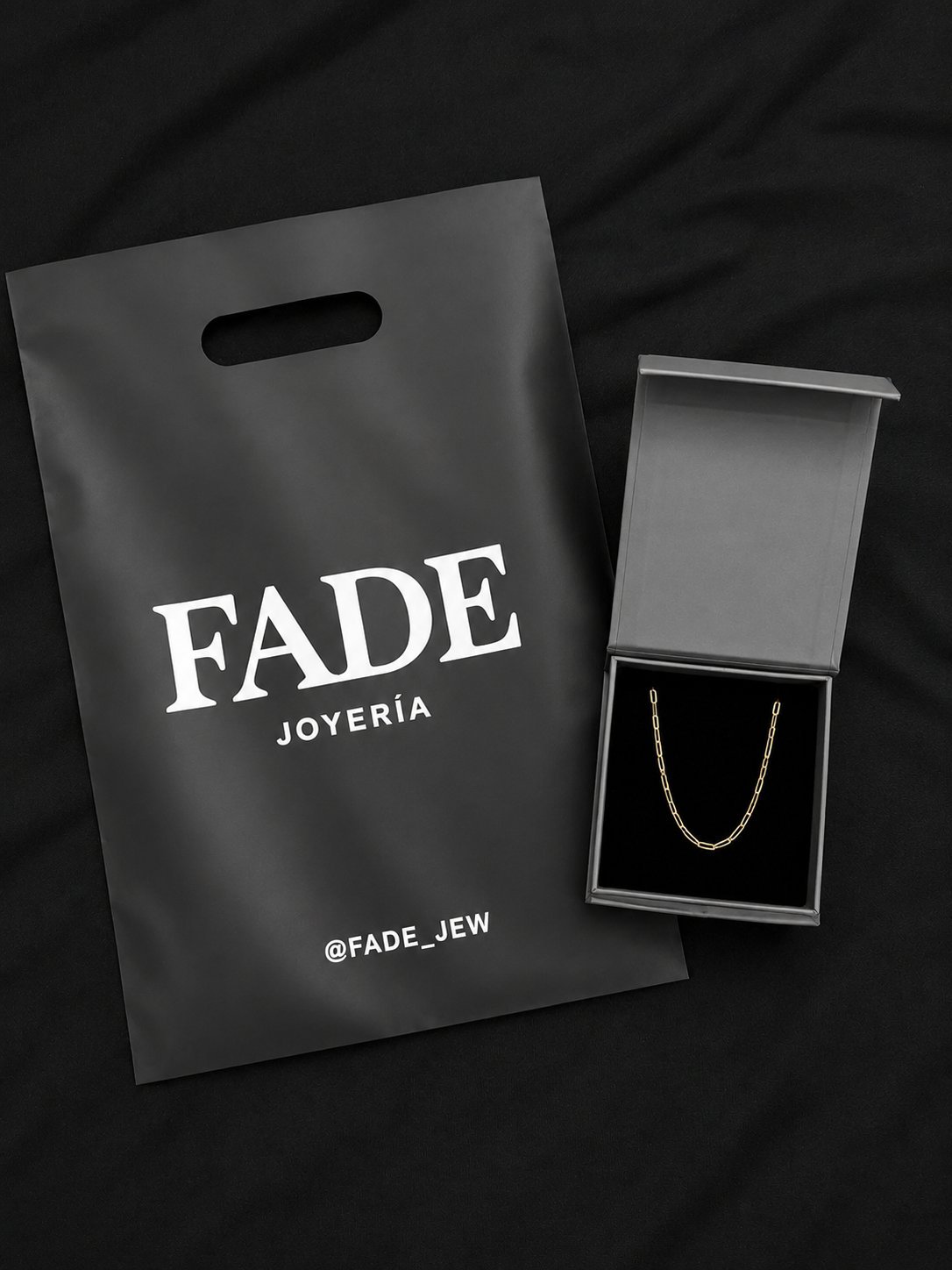 FADE Joyeria jewelry packaging with black branded shopping bag and open gray box containing silver chain necklace on dark background