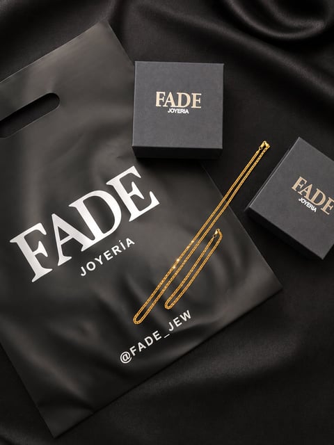FADE Joyería branded jewelry packaging on black fabric, featuring boxes and a black pouch with gold chain details