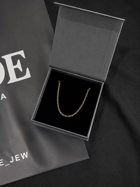 Gold chain necklace displayed in an open gray gift box on dark packaging labeled jewelry